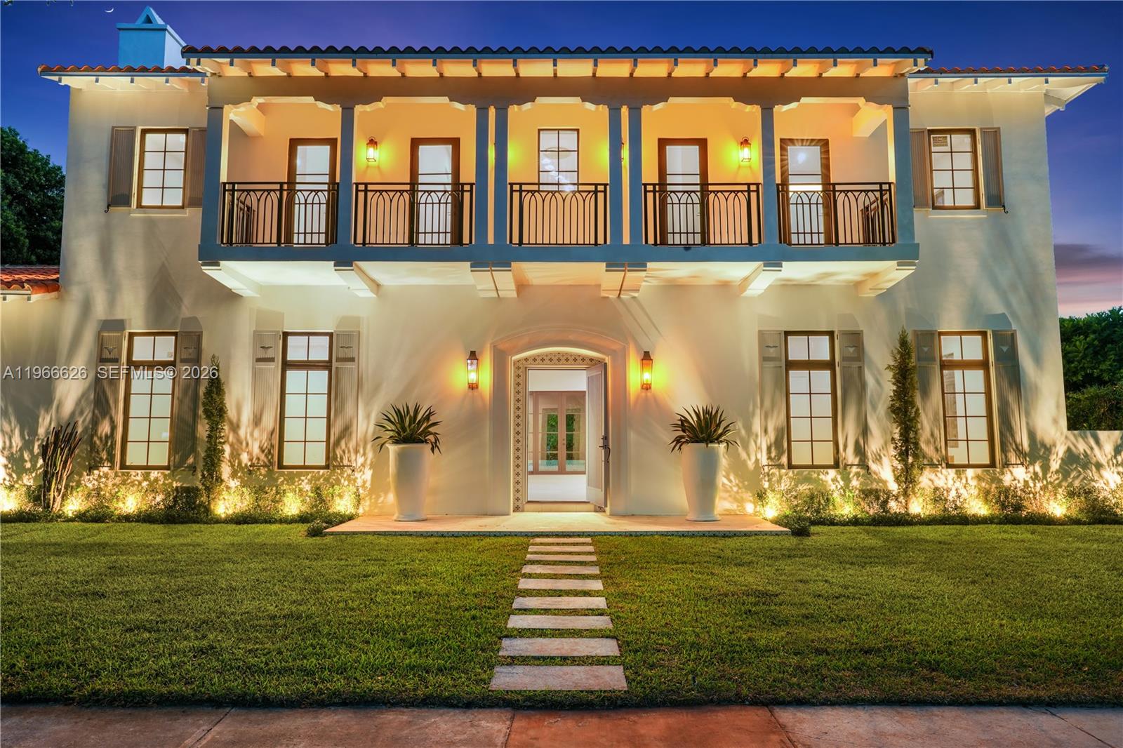 A two-story Mediterranean-style house features a balcony, arched entryway, and symmetrical windows at twilight — 1514 Consolata Ave, Coral Gables FL 33146, CORAL GABLES, FL