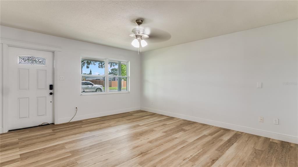 An empty room features light wood-look flooring, white walls, a ceiling fan, and a front door — 4294 NIMONS STREET, ORLANDO, FL