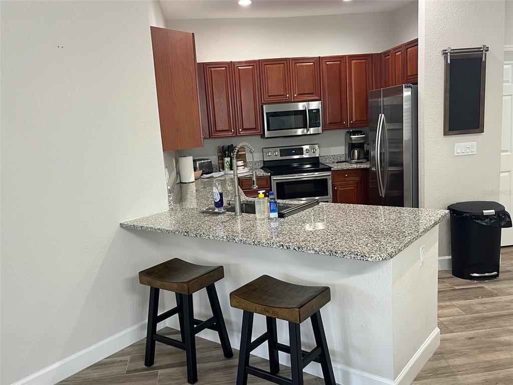 A kitchen features granite countertops, dark wood cabinetry, stainless steel appliances, and two bar stools — 240 W END DRIVE UNIT 821, PUNTA GORDA, FL