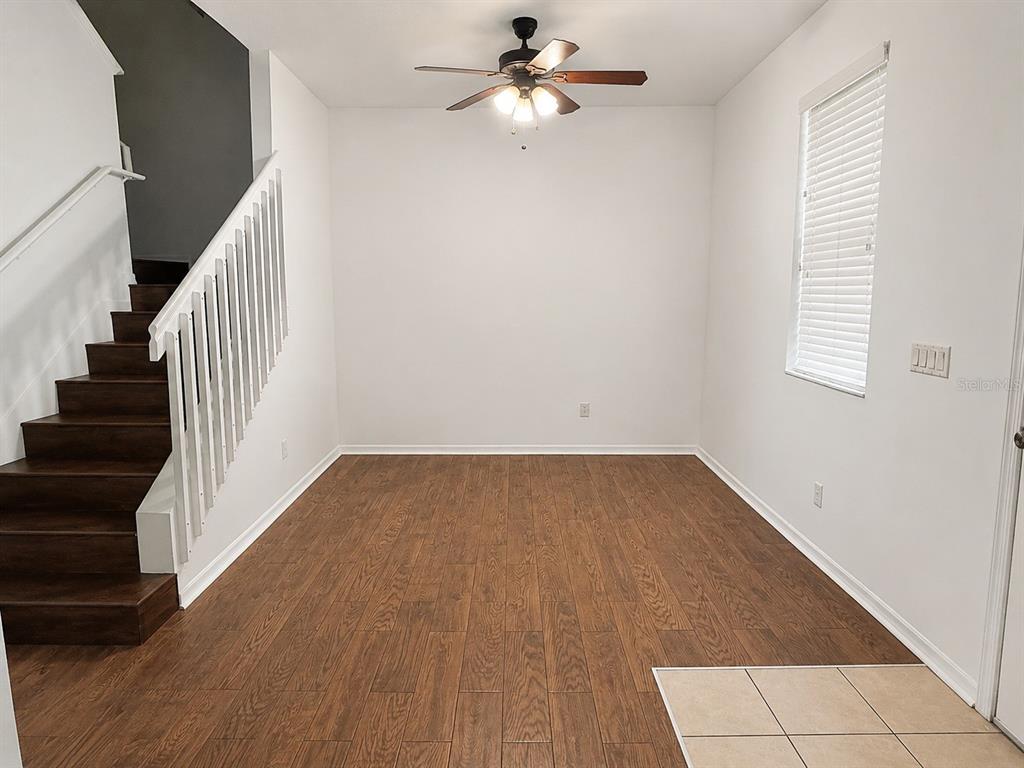 An empty room with wood-look flooring, a ceiling fan, and a staircase with white railings — 4907 TERRAPIN BOULEVARD, ST CLOUD, FL