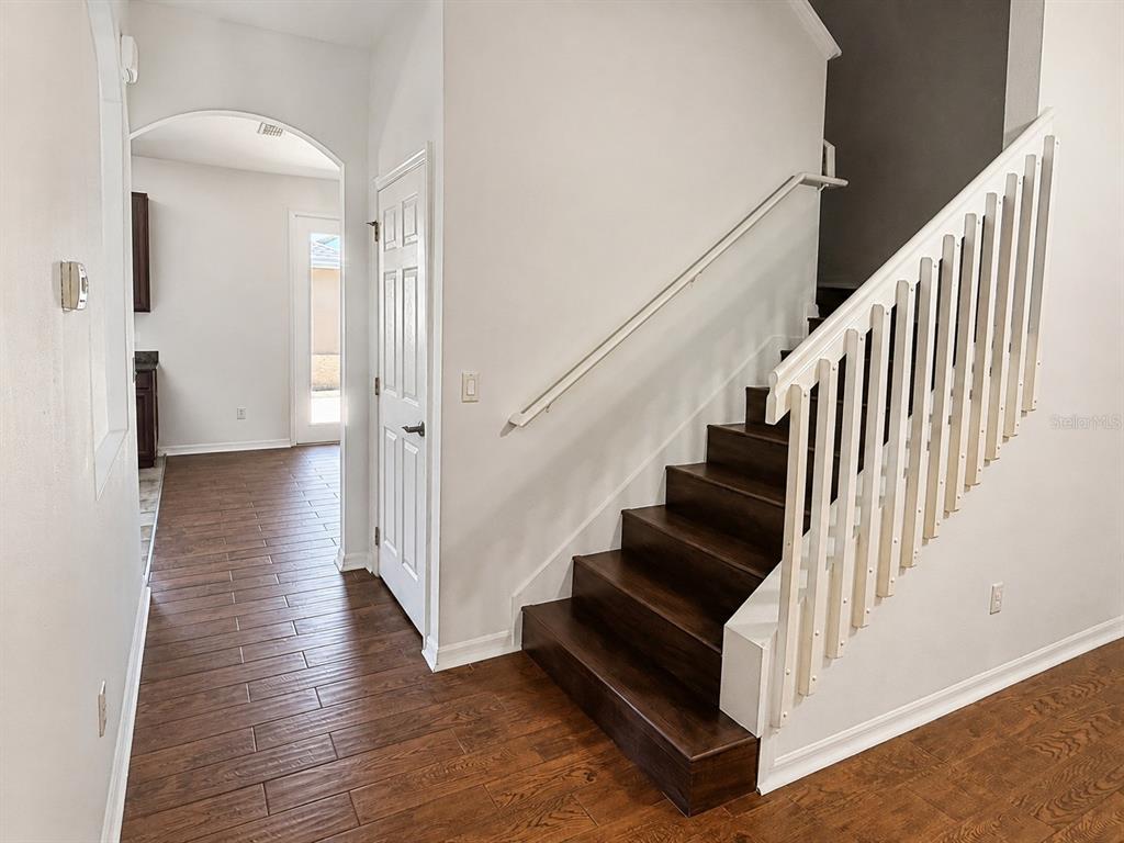 A staircase with dark wood treads and white railings sits beside a hallway with wood-look flooring — 4907 TERRAPIN BOULEVARD, ST CLOUD, FL