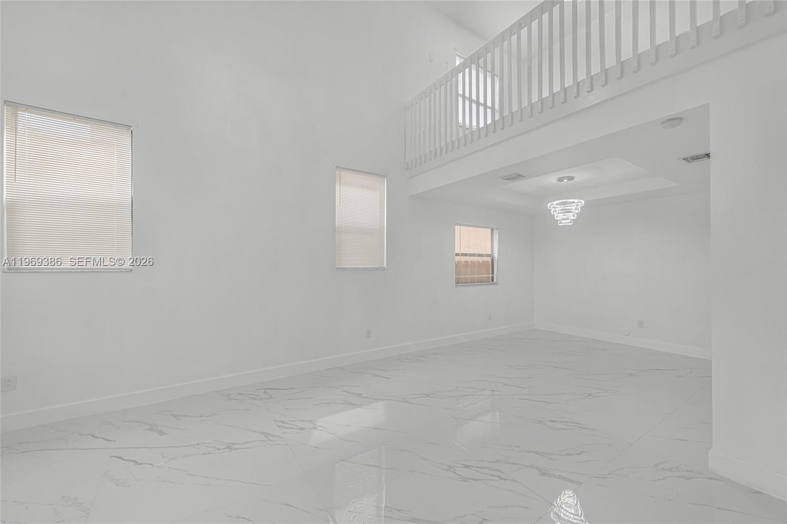 A spacious living room features white walls, marble-look tile flooring, and a second-story balcony railing — 642 SE 37th PL, Homestead FL 33033, HOMESTEAD, FL
