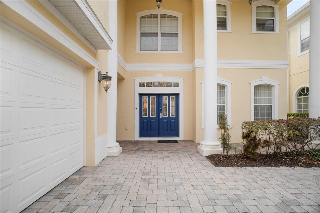 A two-story house exterior features a blue double front door, white columns, and a paver driveway — 7388 GATHERING COURT, REUNION, FL