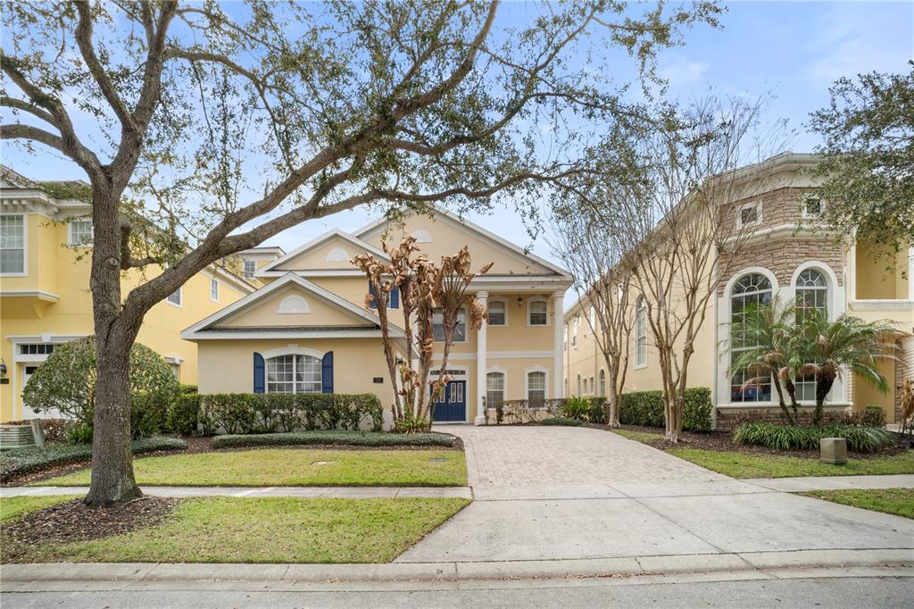 A two-story yellow house with a paved driveway and a large tree in the front yard — 7388 GATHERING COURT, REUNION, FL
