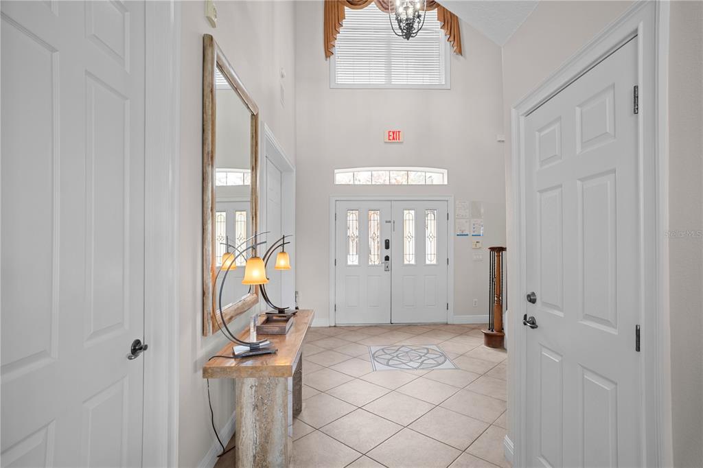 A high-ceilinged foyer features tile flooring, a console table with lamps, and double front doors — 7388 GATHERING COURT, REUNION, FL
