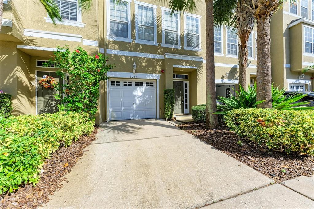 A tan townhouse exterior features a white garage door, a front entrance, and landscaped bushes — 3047 POINTEVIEW DRIVE, TAMPA, FL