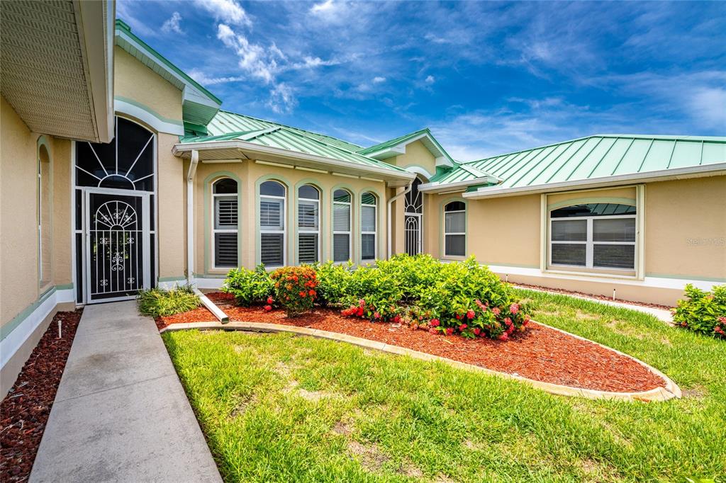 A tan house with a green metal roof and a landscaped front garden — 1611 ATARES DRIVE Unit 111, PUNTA GORDA, FL