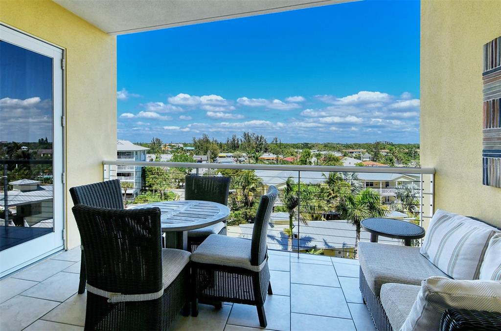 A balcony with wicker furniture, a table, and a view of surrounding houses and trees — 915 SEASIDE DRIVE UNIT 504, Weeks 6-7, SARASOTA, FL