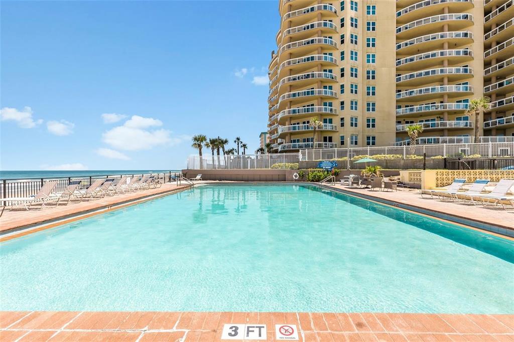 A rectangular swimming pool sits on a patio next to a tall beachfront resort building — 1909 S ATLANTIC AVENUE UNIT 411 & 412, DAYTONA BEACH, FL