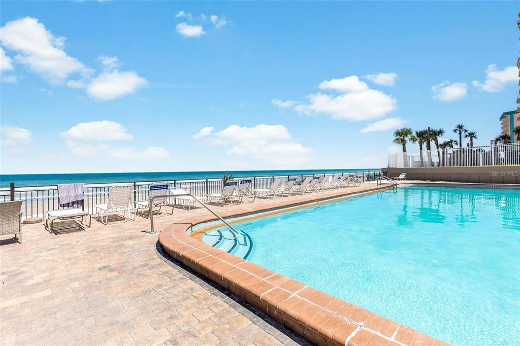 An outdoor swimming pool overlooks the ocean with lounge chairs on a paved deck — 1909 S ATLANTIC AVENUE UNIT 411 & 412, DAYTONA BEACH, FL