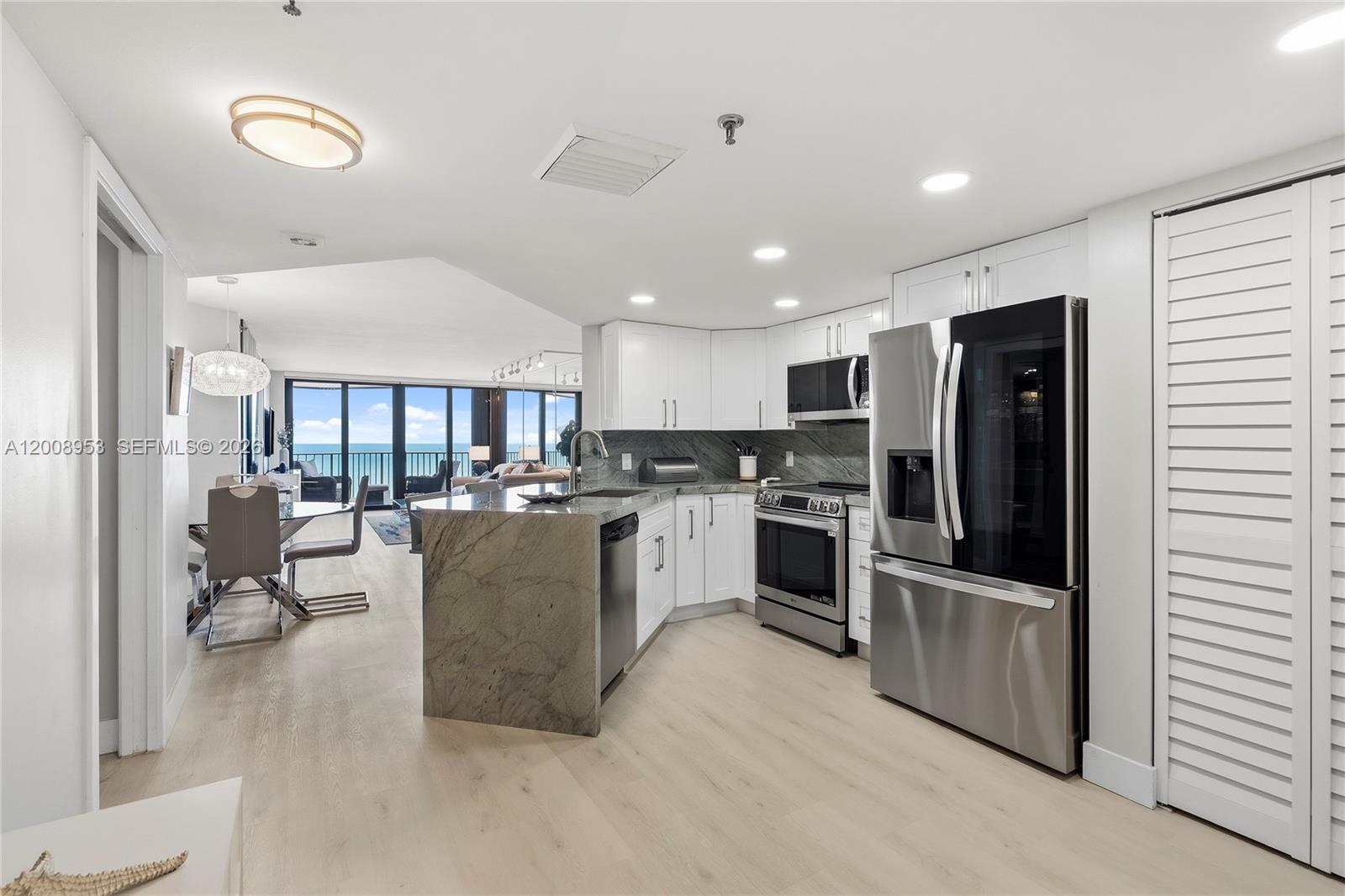 A modern kitchen with white cabinets and stone countertops opens to a dining area — 9650 S Ocean Dr # 1509, Jensen Beach FL 34957, JENSEN BEACH, FL