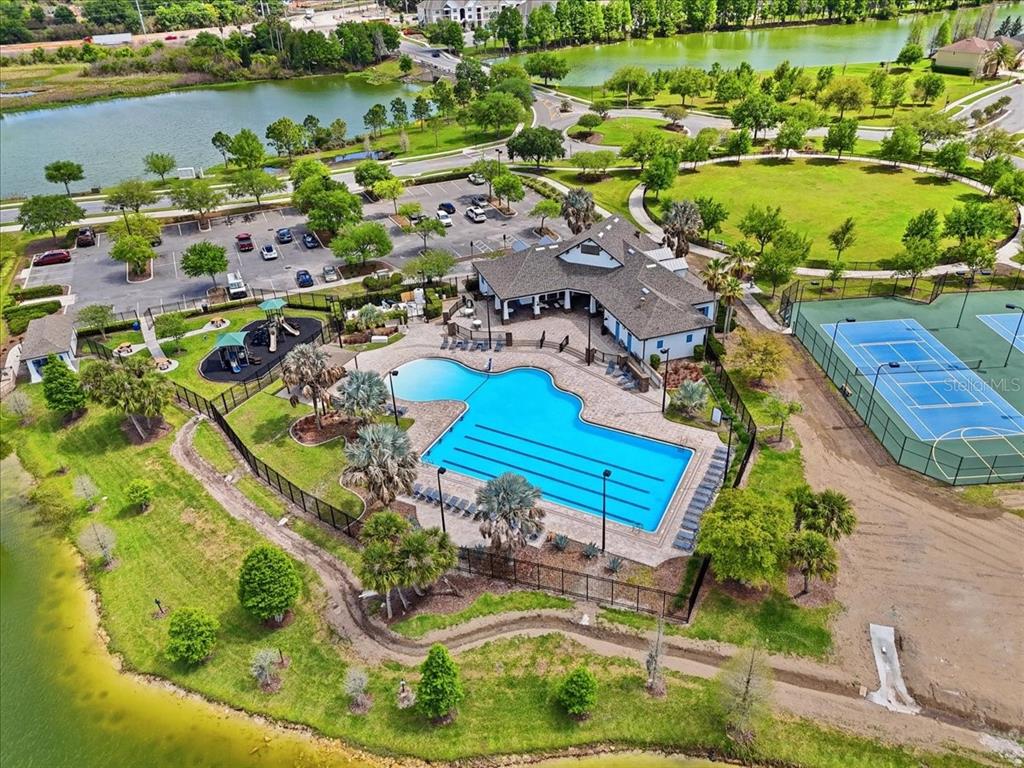 An aerial view shows a community pool, clubhouse, playground, and tennis courts near a lake — 6431 COMO PLACE, LAKELAND, FL