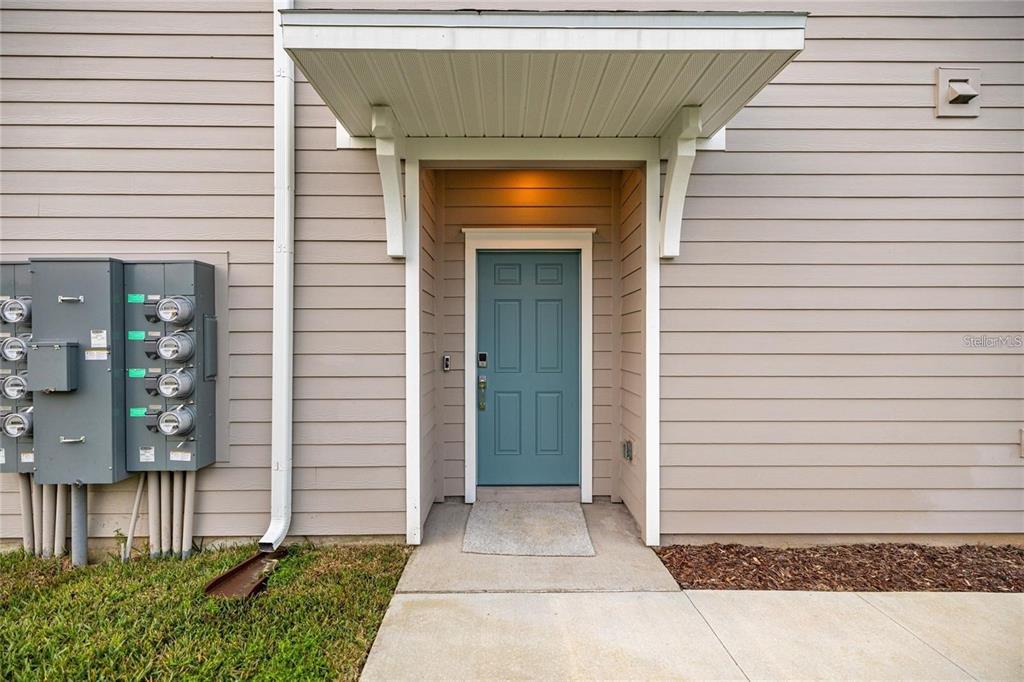 A teal front door is centered under a small porch awning on a beige building — 3644 SE 37TH COURT, OCALA, FL