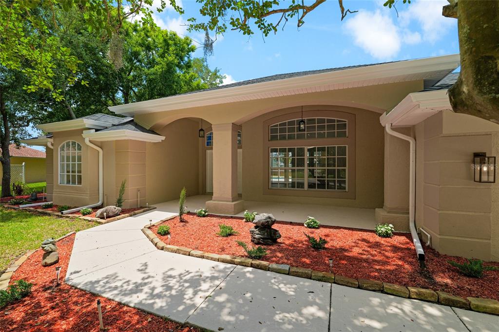A tan stucco house exterior features a covered entryway, a large arched window, and landscaping — 3519 SANDBURG LOOP, PLANT CITY, FL