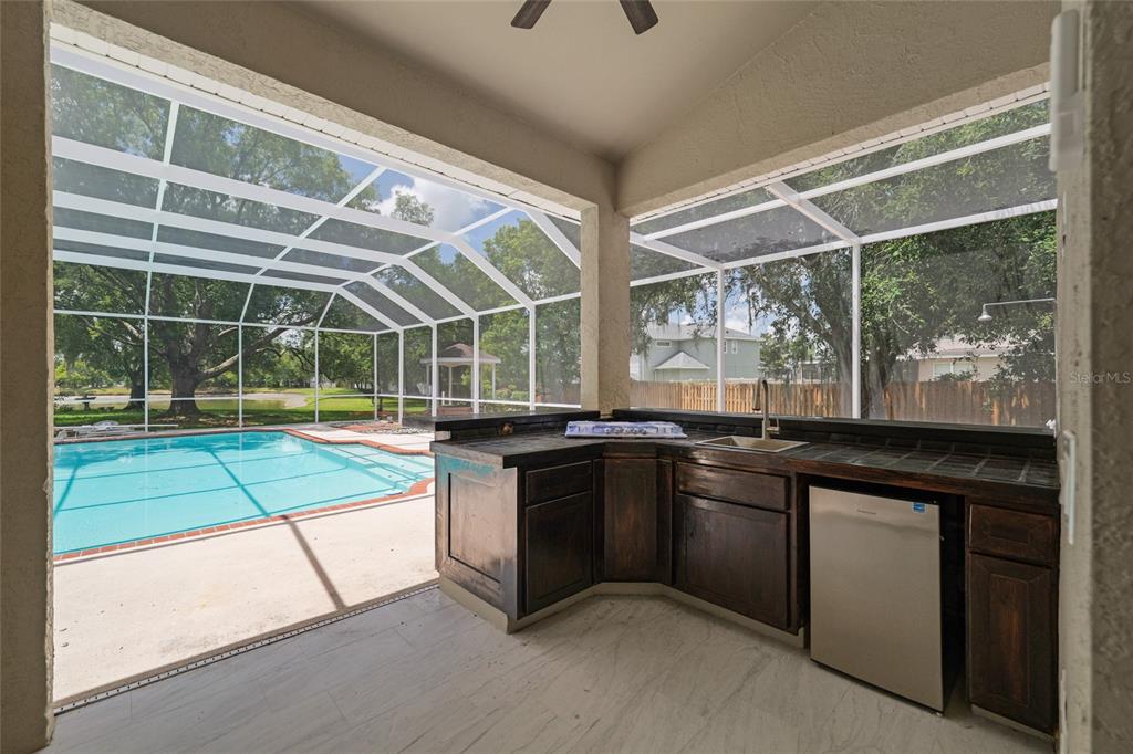 A covered patio features a tiled outdoor kitchen with a sink and a swimming pool — 3519 SANDBURG LOOP, PLANT CITY, FL