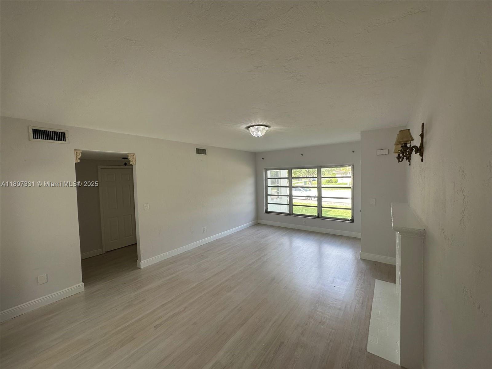 A living room features light wood-look flooring, a fireplace, and a large window — 3621 Ponce De Leon Blvd, Coral Gables FL 33134, CORAL GABLES, FL