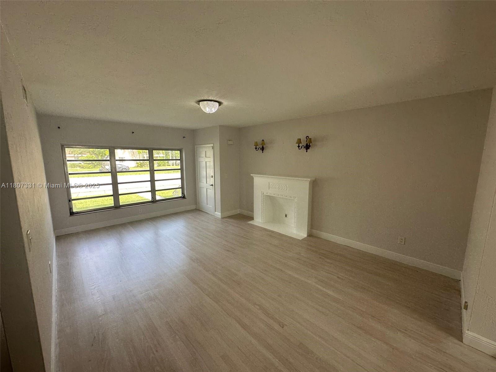 A living room features light wood-look flooring, a white fireplace, and a large window — 3621 Ponce De Leon Blvd, Coral Gables FL 33134, CORAL GABLES, FL