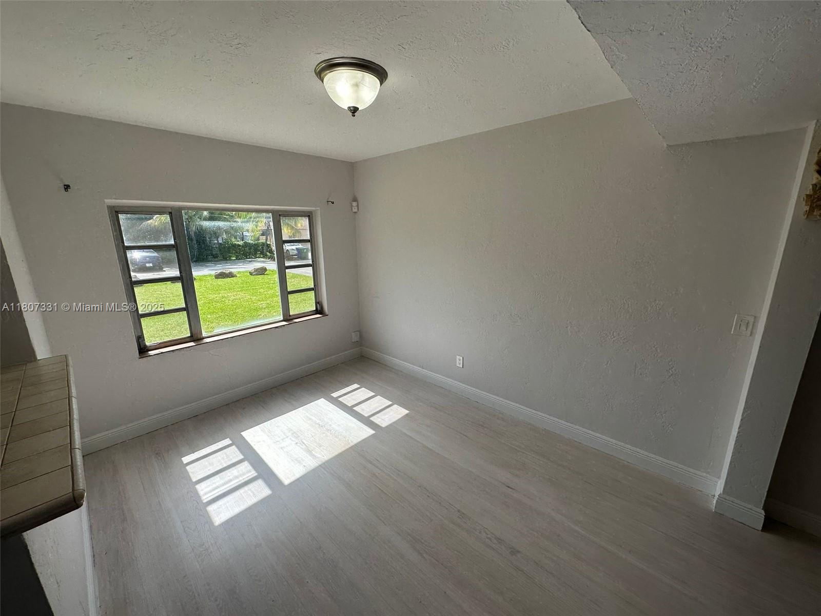 An empty room features light-colored wood flooring, a large window, and a ceiling light fixture — 3621 Ponce De Leon Blvd, Coral Gables FL 33134, CORAL GABLES, FL