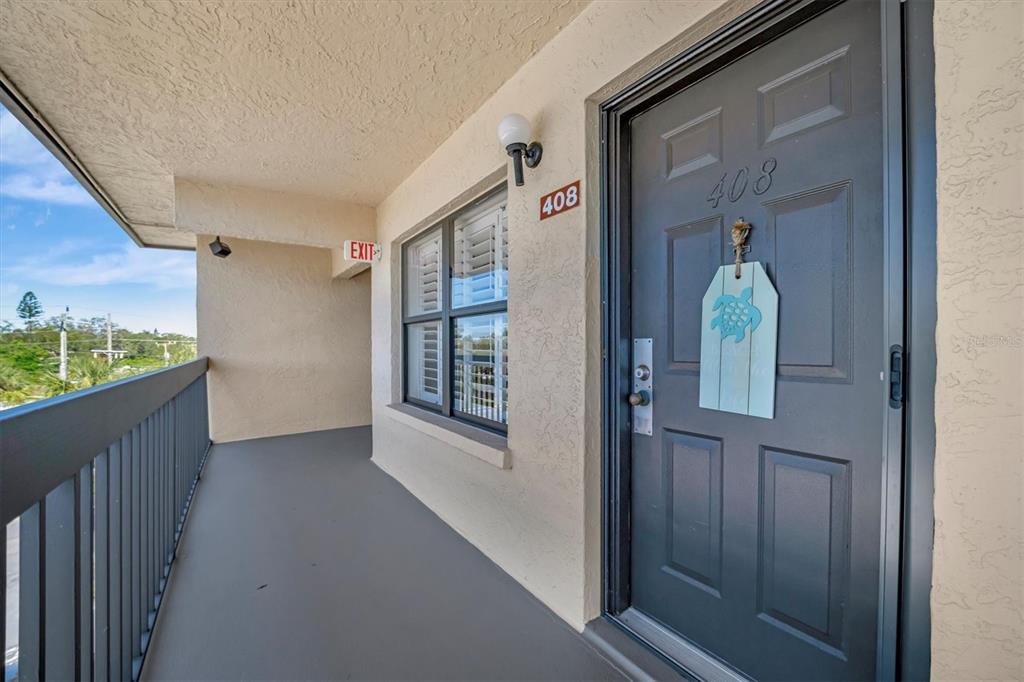 A gray front door with a turtle sign leads to an outdoor balcony walkway — 625 30TH AVENUE W UNIT G408, BRADENTON, FL
