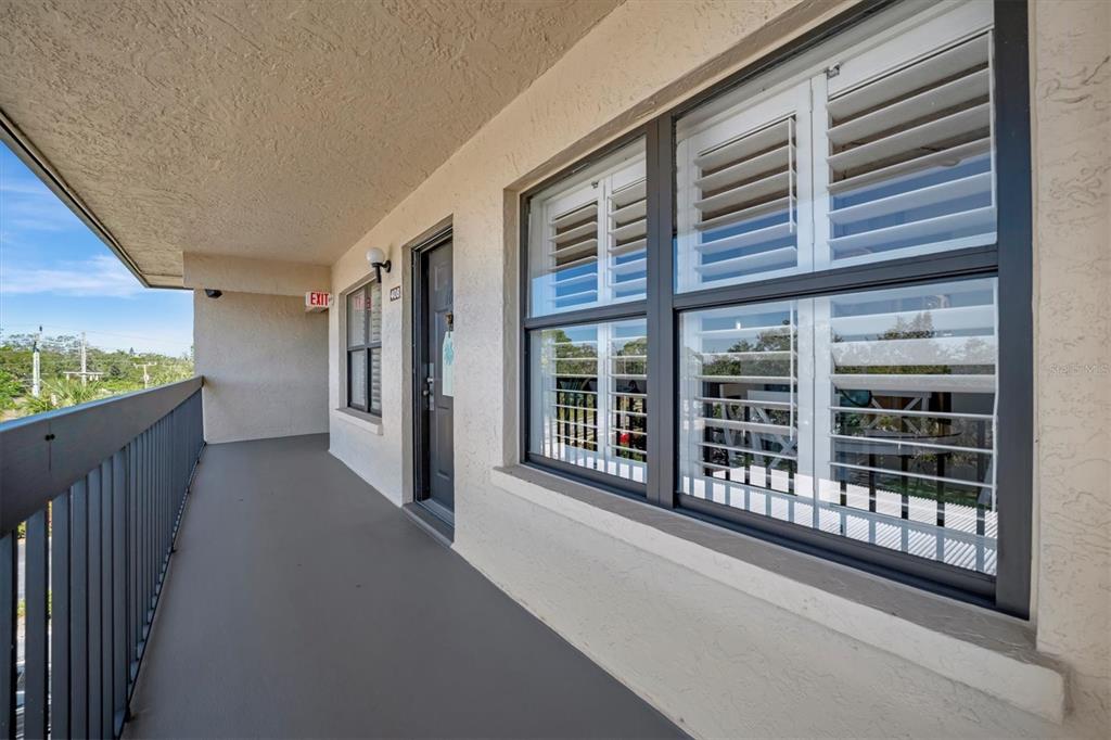 An exterior walkway features a dark door, a large window with shutters, and a metal railing — 625 30TH AVENUE W UNIT G408, BRADENTON, FL