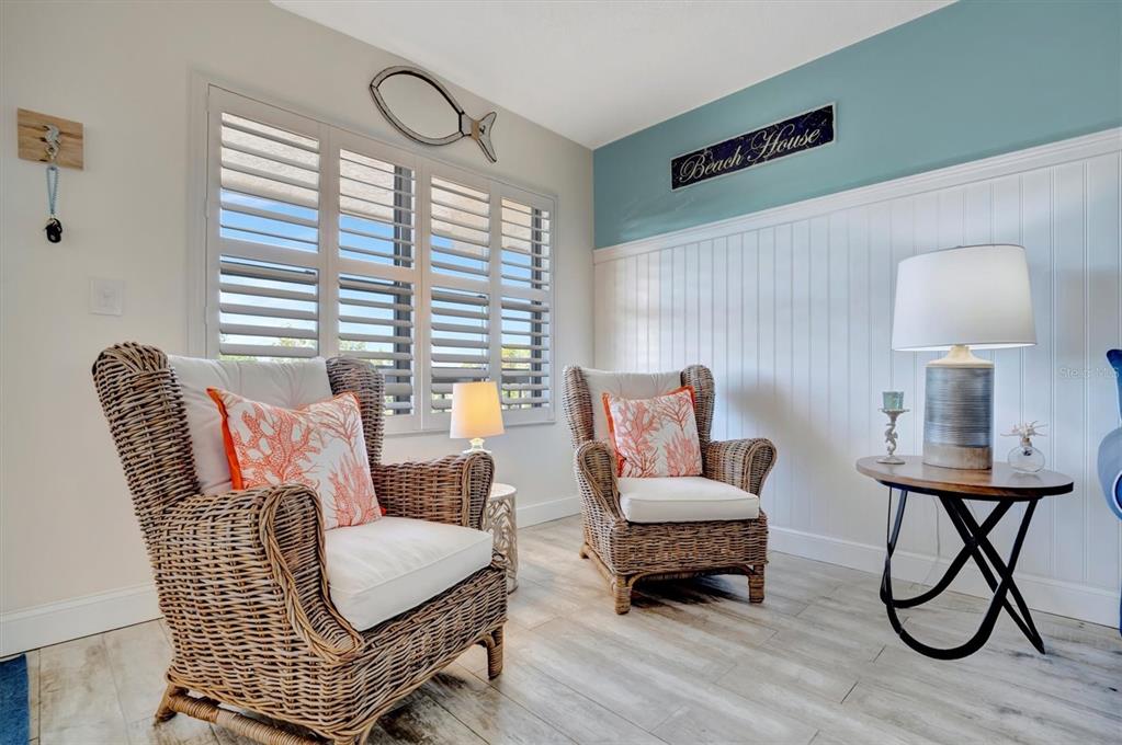 Two wicker armchairs with orange coral-patterned pillows sit in a room with wood-look flooring — 625 30TH AVENUE W UNIT G408, BRADENTON, FL