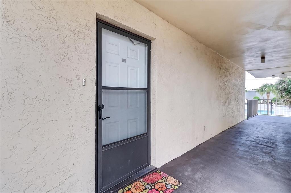 A dark-framed storm door leads to a covered exterior walkway with textured stucco walls — 1130 N LAKE PARKER AVENUE UNIT E233, LAKELAND, FL