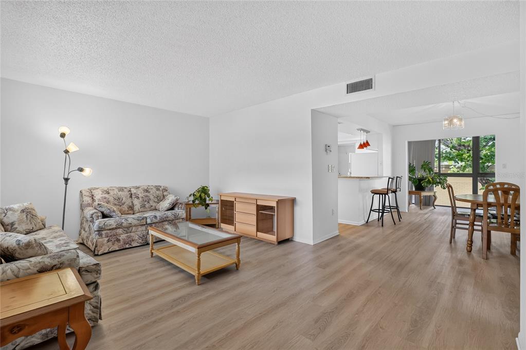 A living room with light wood flooring, floral sofas, and an adjacent dining area — 1130 N LAKE PARKER AVENUE UNIT E233, LAKELAND, FL