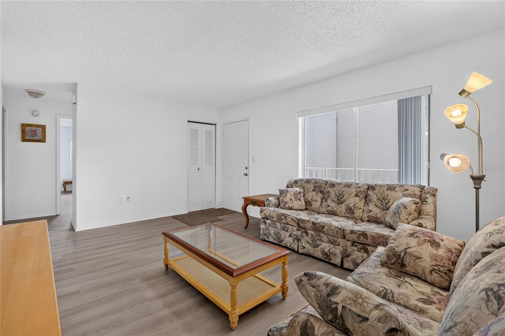 A living room features wood-look flooring, a floral sofa, a glass coffee table, and white walls — 1130 N LAKE PARKER AVENUE UNIT E233, LAKELAND, FL