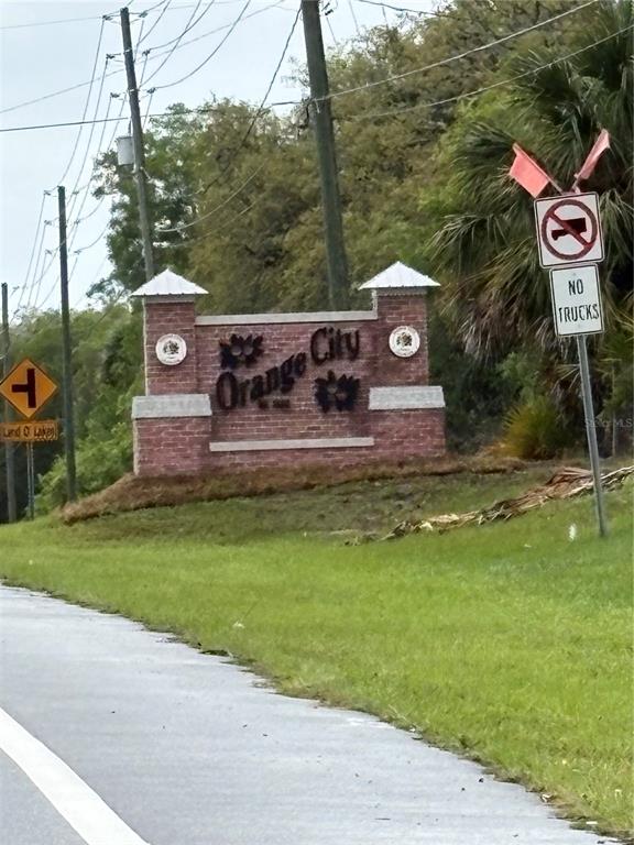 A brick monument sign for Orange City stands beside a road with traffic signs — 1425 E GRAVES AVENUE, ORANGE CITY, FL