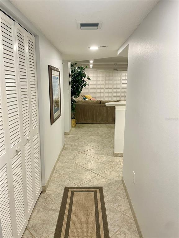 A hallway with white louvered closet doors leads to a living area with tiled floors — 1290 GULF BOULEVARD UNIT 307, CLEARWATER, FL