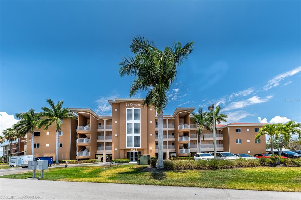 A multi-story tan apartment building with palm trees and a parking lot in front — 3322 PURPLE MARTIN DR UNIT 132, PUNTA GORDA, FL