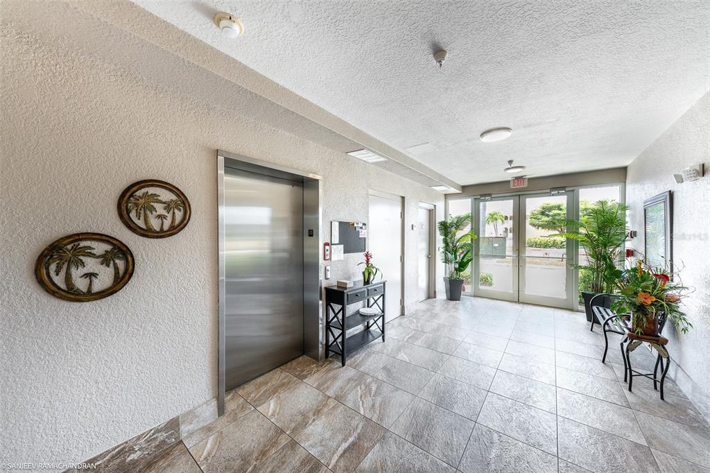 A tiled building lobby features a stainless steel elevator, a console table, and glass doors — 3322 PURPLE MARTIN DR UNIT 132, PUNTA GORDA, FL