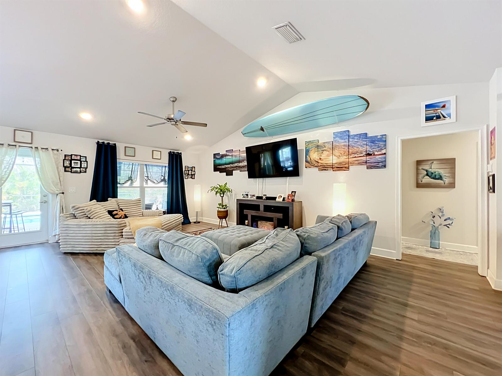 A living room features a blue sectional sofa, a surfboard wall display, and wood flooring — 1574 Quiescent Lane, Sebastian FL 32958, SEBASTIAN, FL