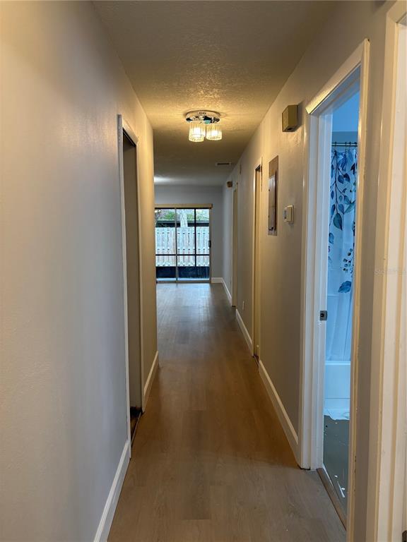 A hallway with light wood-look flooring leads toward a sliding glass door at the end — 7733 COUNTRY PLACE UNIT G2, WINTER PARK, FL
