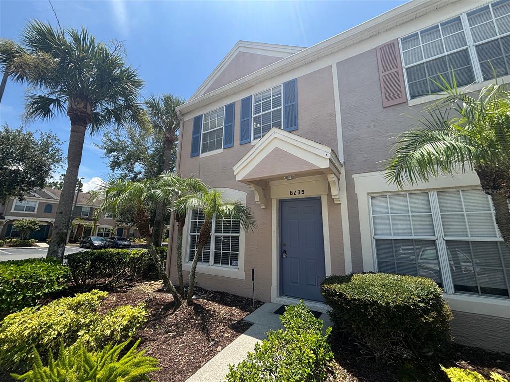 A two-story townhouse exterior features a blue front door, tan stucco siding, and palm trees — 6235 BAYSIDE KEY DRIVE, TAMPA, FL