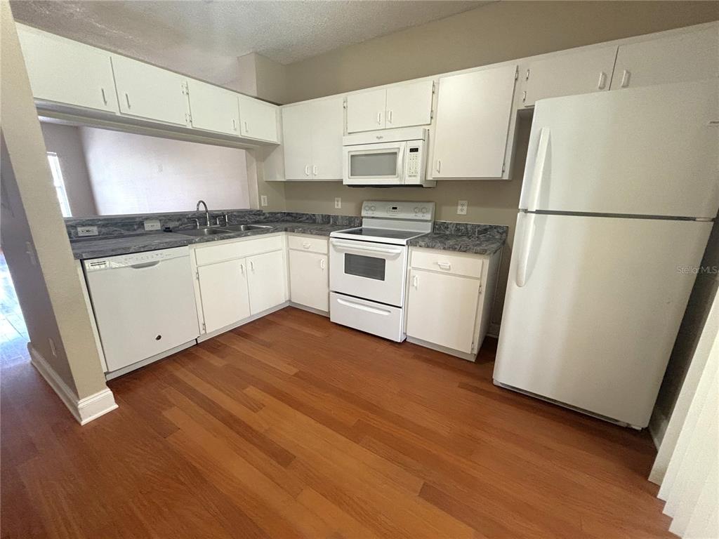 A kitchen features white cabinets, white appliances, gray laminate countertops, and wood-look flooring — 6235 BAYSIDE KEY DRIVE, TAMPA, FL