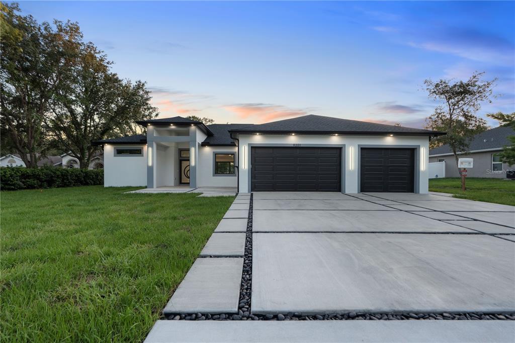 A modern single-story house with a white exterior, dark garage doors, and a paved driveway — 9201 NIGHTINGALE ROAD, WEEKI WACHEE, FL