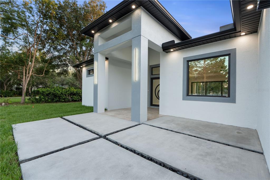 A modern white house exterior features a concrete paver walkway and a covered entryway — 9201 NIGHTINGALE ROAD, WEEKI WACHEE, FL