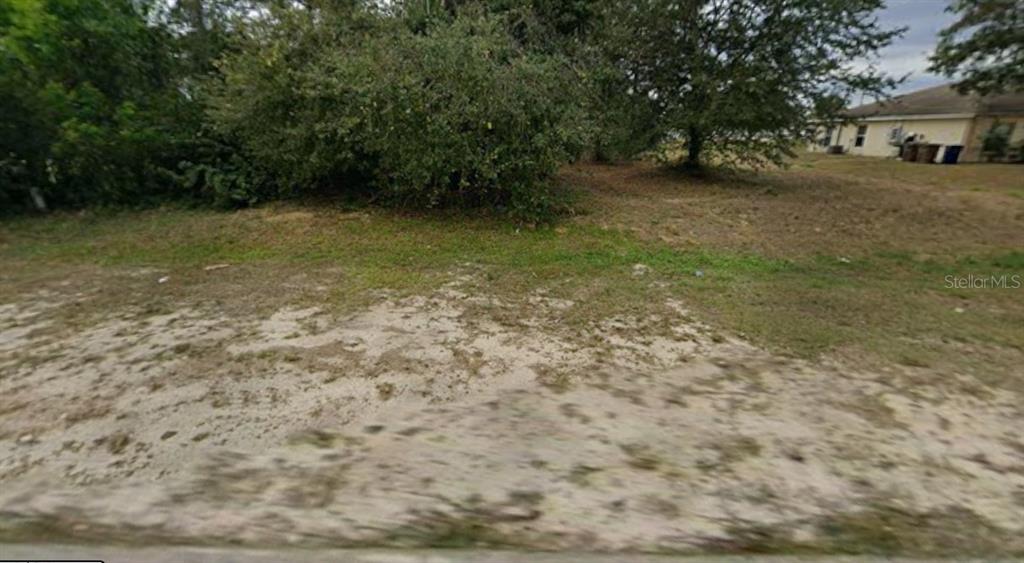 A vacant, grassy lot with sandy ground and scattered trees in front of a house — 138 GRETCHEN AVENUE S, LEHIGH ACRES, FL