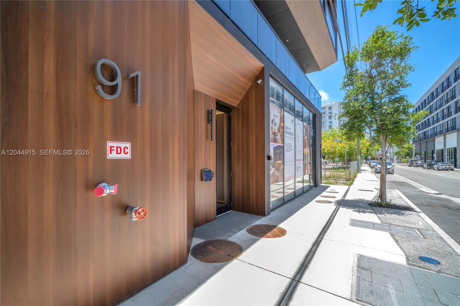 The exterior of a modern building features wood-paneled walls, a fire department connection, and a sidewalk — 91 NW 27th St # 503, Miami FL 33127, MIAMI, FL