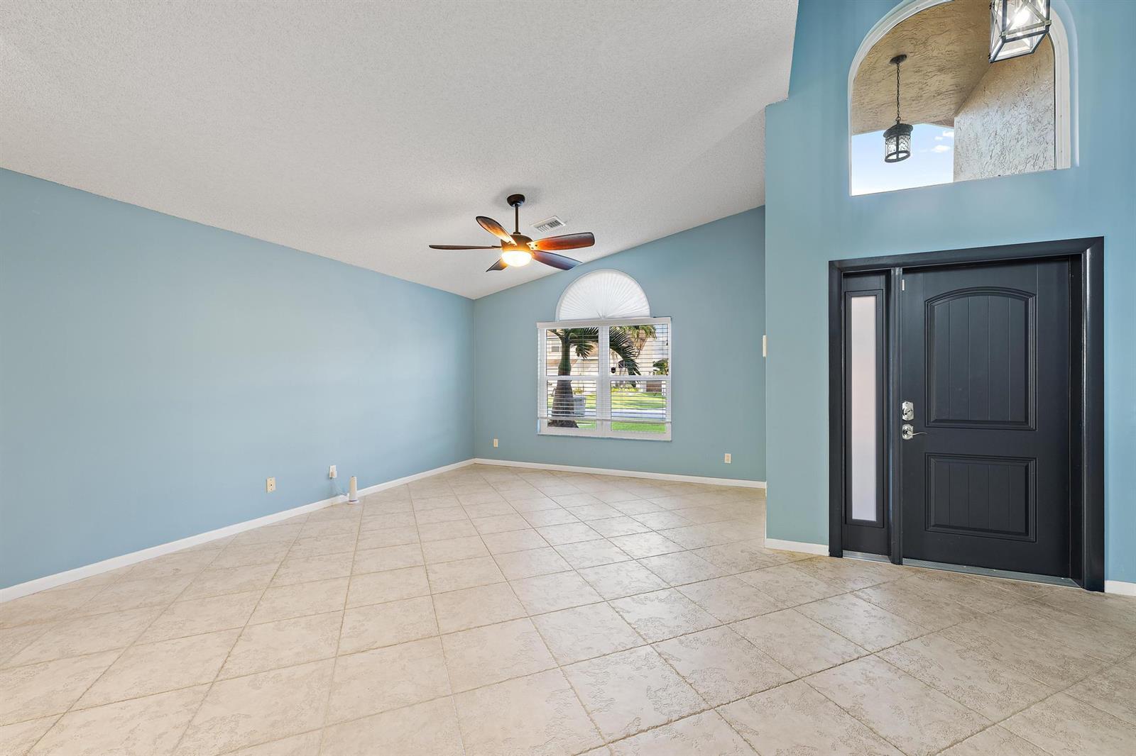 A living room with light blue walls, tile flooring, a ceiling fan, and an entryway — 8657 Tourmaline Boulevard, Boynton Beach FL 33472, BOYNTON BEACH, FL