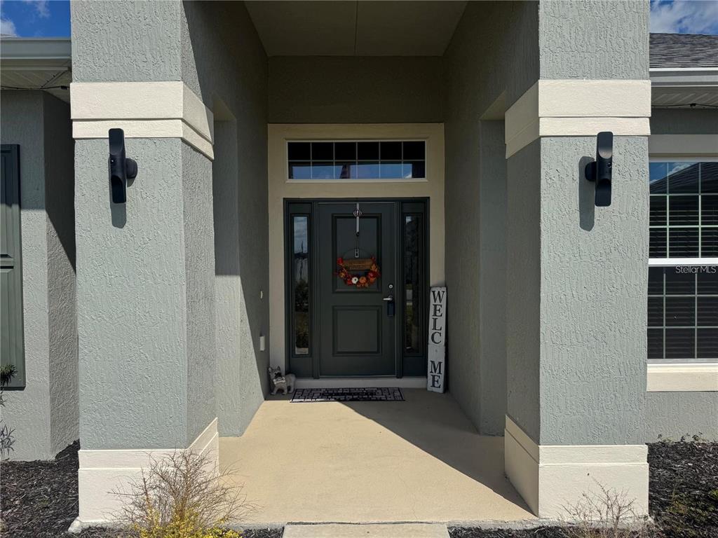 A gray front door with sidelights and a transom window sits under a covered porch — 5123 SW 91ST STREET, OCALA, FL