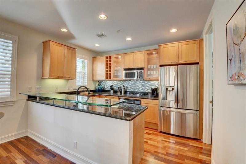A kitchen features light wood cabinets, stainless steel appliances, and a glass-topped breakfast bar — 306 E Mallory Circle, Delray Beach FL 33483, DELRAY BEACH, FL