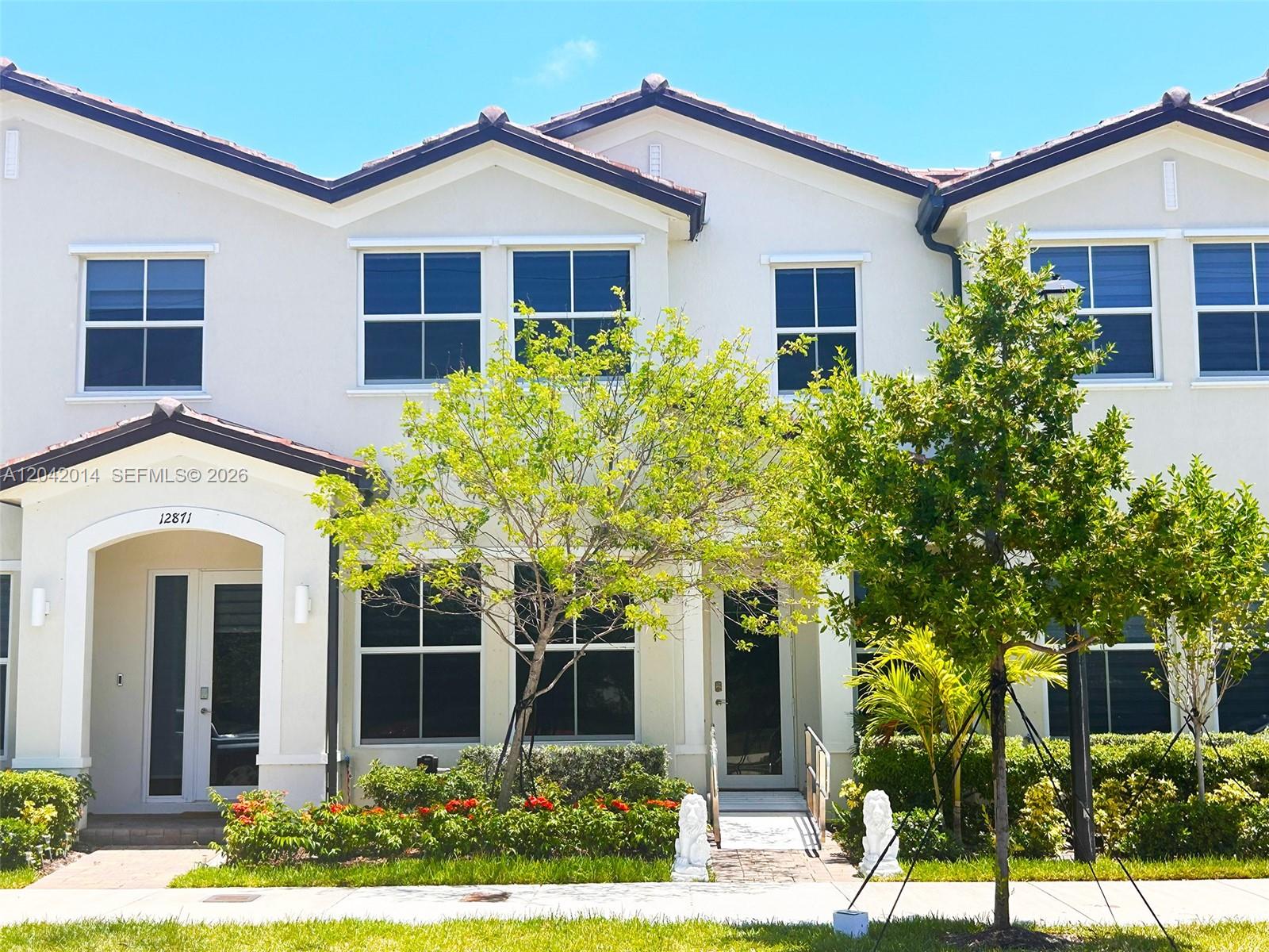 A two-story townhouse exterior features a beige facade, tiled roof, and a small front garden — 12867 SW 243rd Ter, Homestead FL 33032, HOMESTEAD, FL