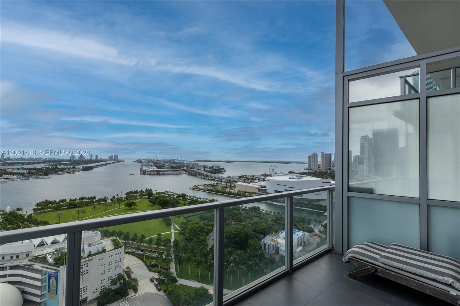 A balcony with a glass railing overlooks a park, a bay, and city buildings — 1100 Biscayne Blvd # 2706, Miami FL 33132, MIAMI, FL