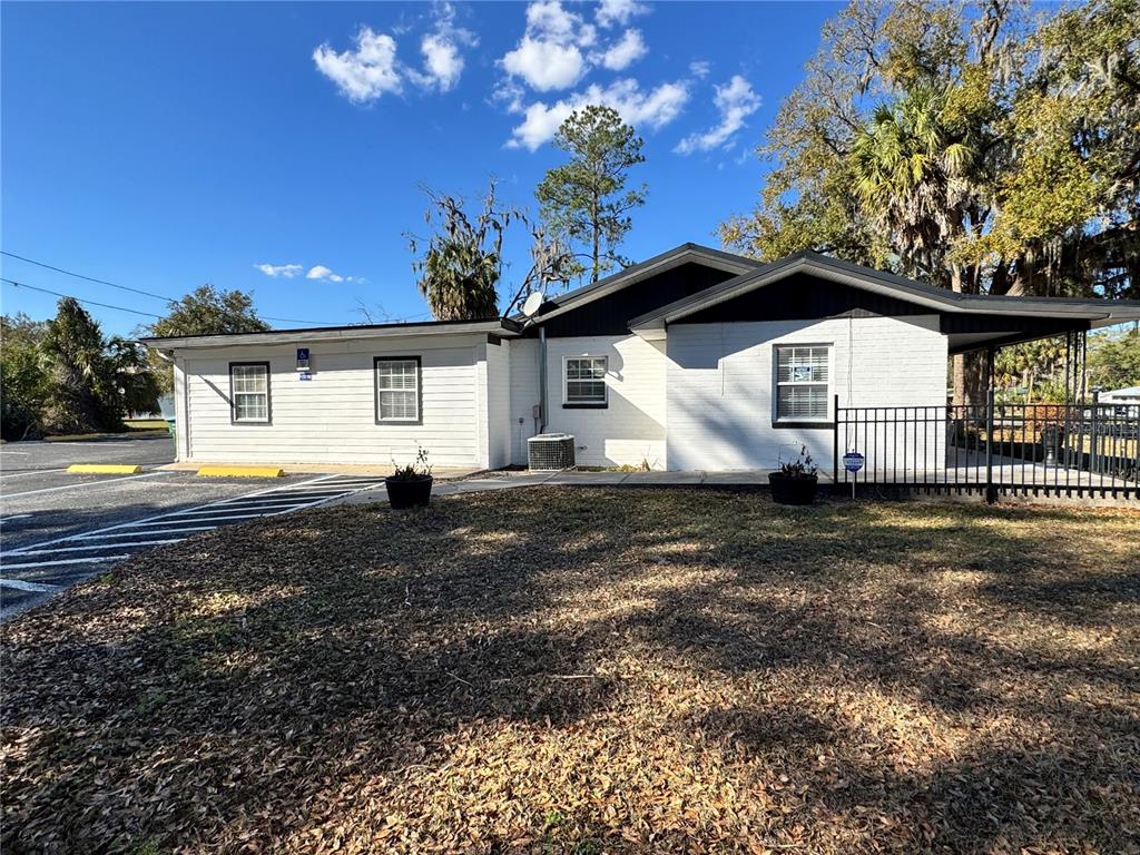 A single-story building with white siding and brick walls sits beside a paved parking lot — 304 NE 1ST STREET, CHIEFLAND, FL