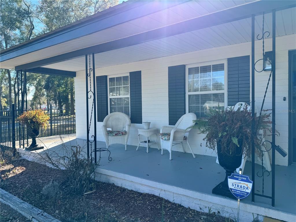 A covered front porch features two white wicker chairs, a small table, and potted plants — 304 NE 1ST STREET, CHIEFLAND, FL