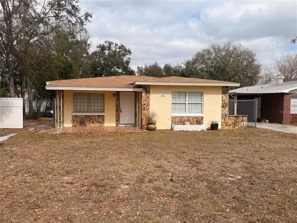 A single-story house with yellow stucco walls, stone accents, and a brown shingled roof — 402 TUSCARORA STREET, LAKELAND, FL
