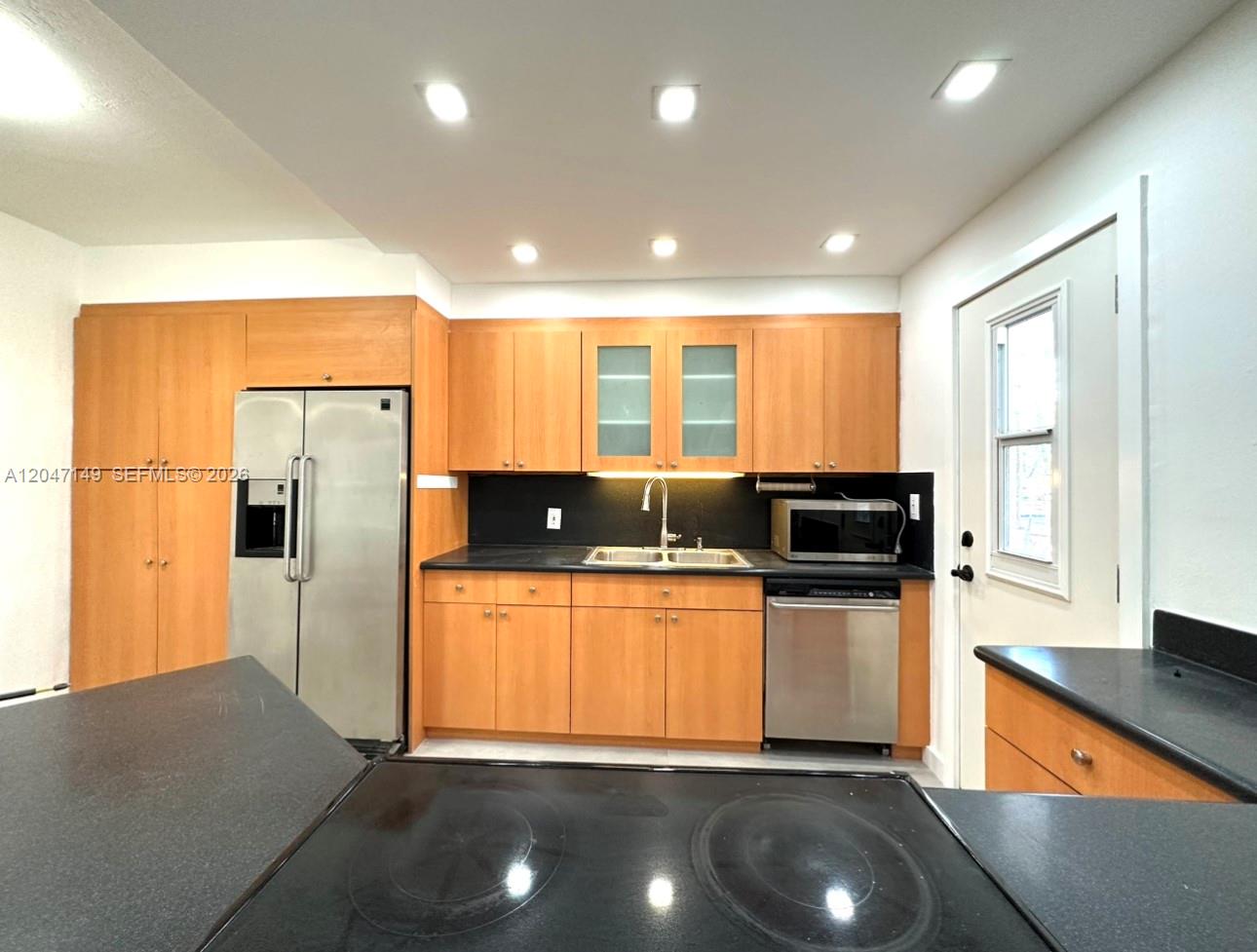 A kitchen features light wood cabinets, black countertops, stainless steel appliances, and recessed lighting — 2924 Day Ave # N114, Miami FL 33133, MIAMI, FL
