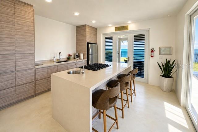 A modern kitchen features a central island with bar seating and a view of the ocean — 14 CAMINO LAS PICUAS, RIO GRANDE, PR